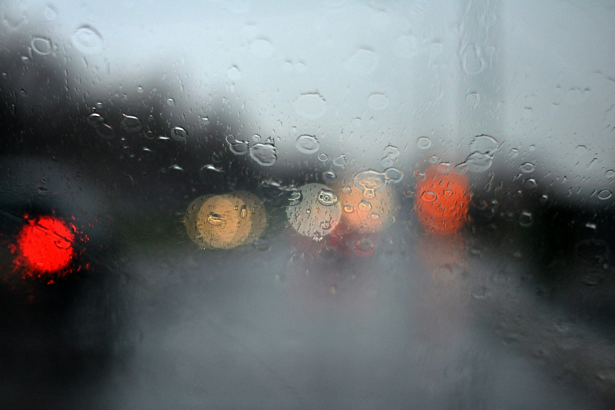 雨に濡れる車のフロントガラス越しに見える街の灯り、雨天の配達をイメージした写真